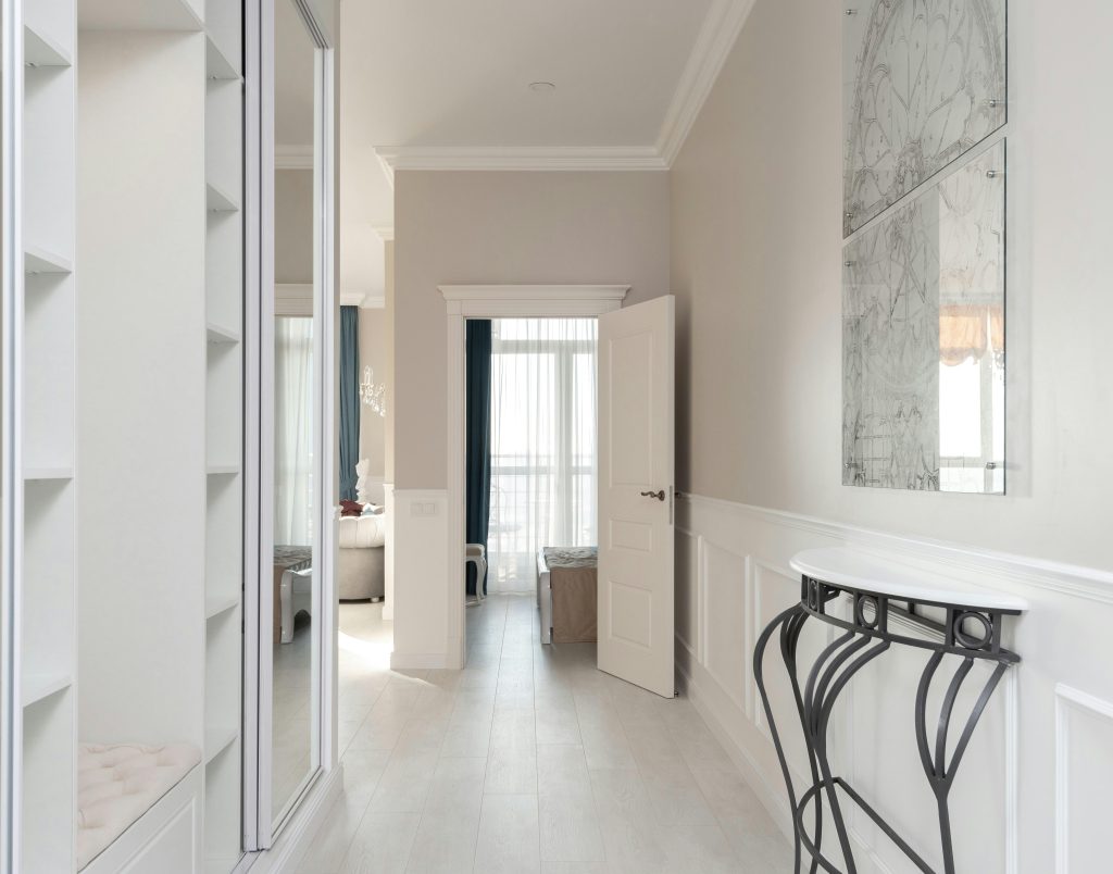 Hallway with empty opened wardrobe and mirror against wall with decorated white shelf in contemporary spacious light flat with rooms Couloir avec armoire ouverte vide et miroir contre le mur avec étagère blanche décorée dans un appartement spacieux et lumineux contemporain avec plusieurs pièces