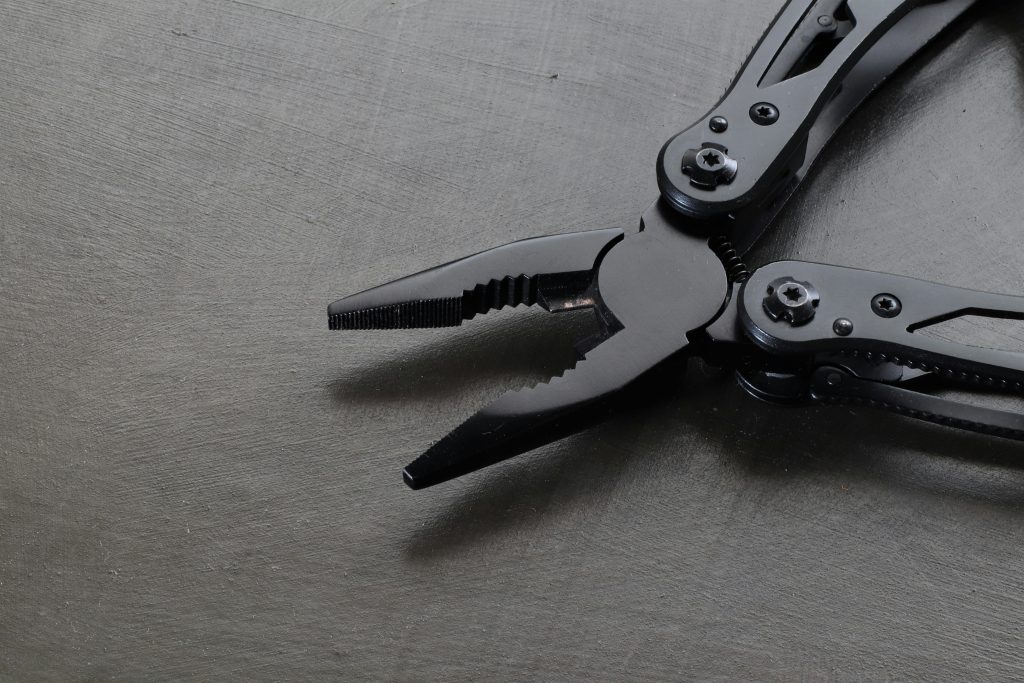 Black metal pliers on a dark surface, emphasizing industrial precision and durability. Des pinces en métal noir sur une surface sombre, mettant l'accent sur la précision industrielle et la durabilité.