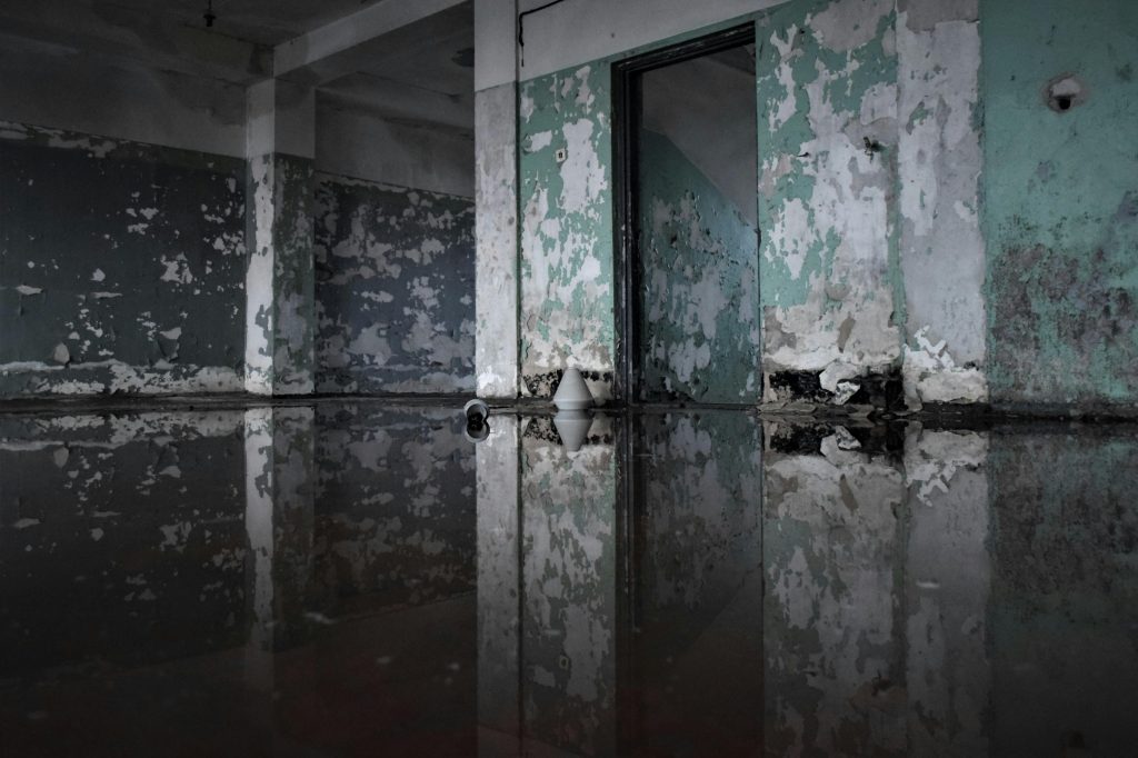 A decaying abandoned room with peeling paint and flooded floor, creating a reflection effect. Une pièce abandonnée en ruine avec de la peinture qui s'écaille et un sol inondé, créant un effet de reflet.