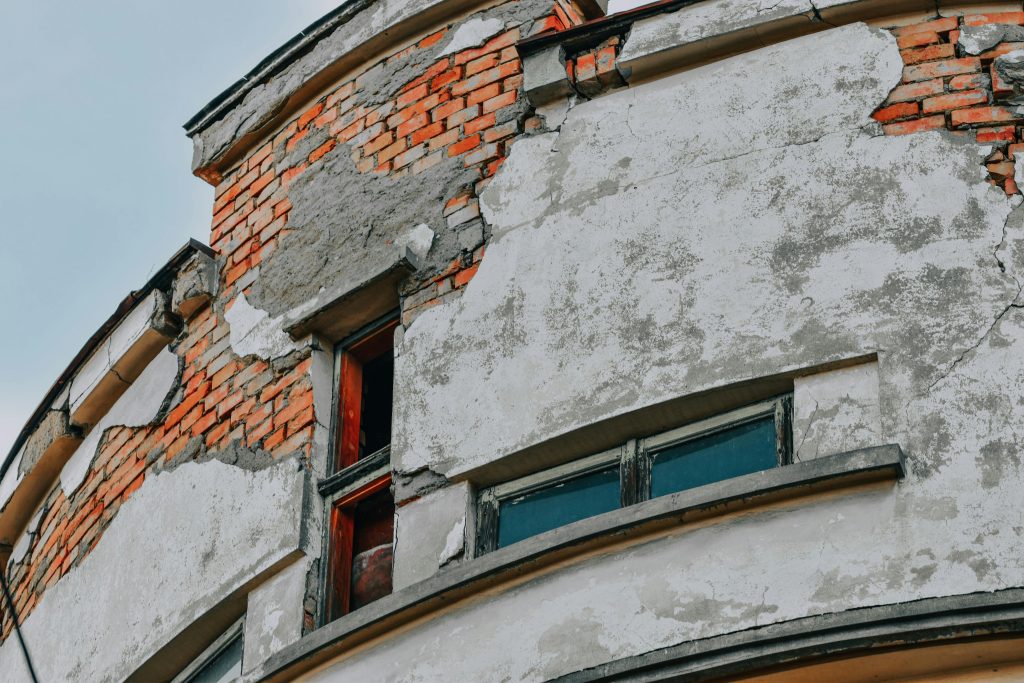 Close-up of a weathered brick building facade showing cracks and deterioration. Gros plan de la façade d'un bâtiment en brique usée montrant des fissures et de la détérioration.