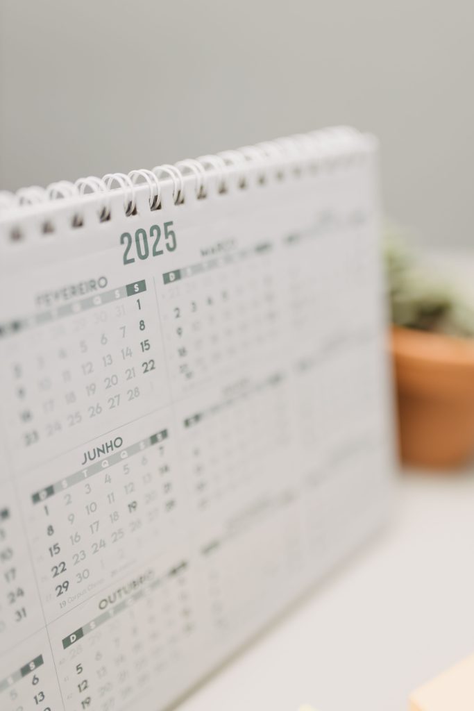 Close-up of a 2025 desk calendar beside a potted succulent on a desk. Gros plan d'un calendrier de bureau 2025 à côté d'une plante grasse en pot sur un bureau.