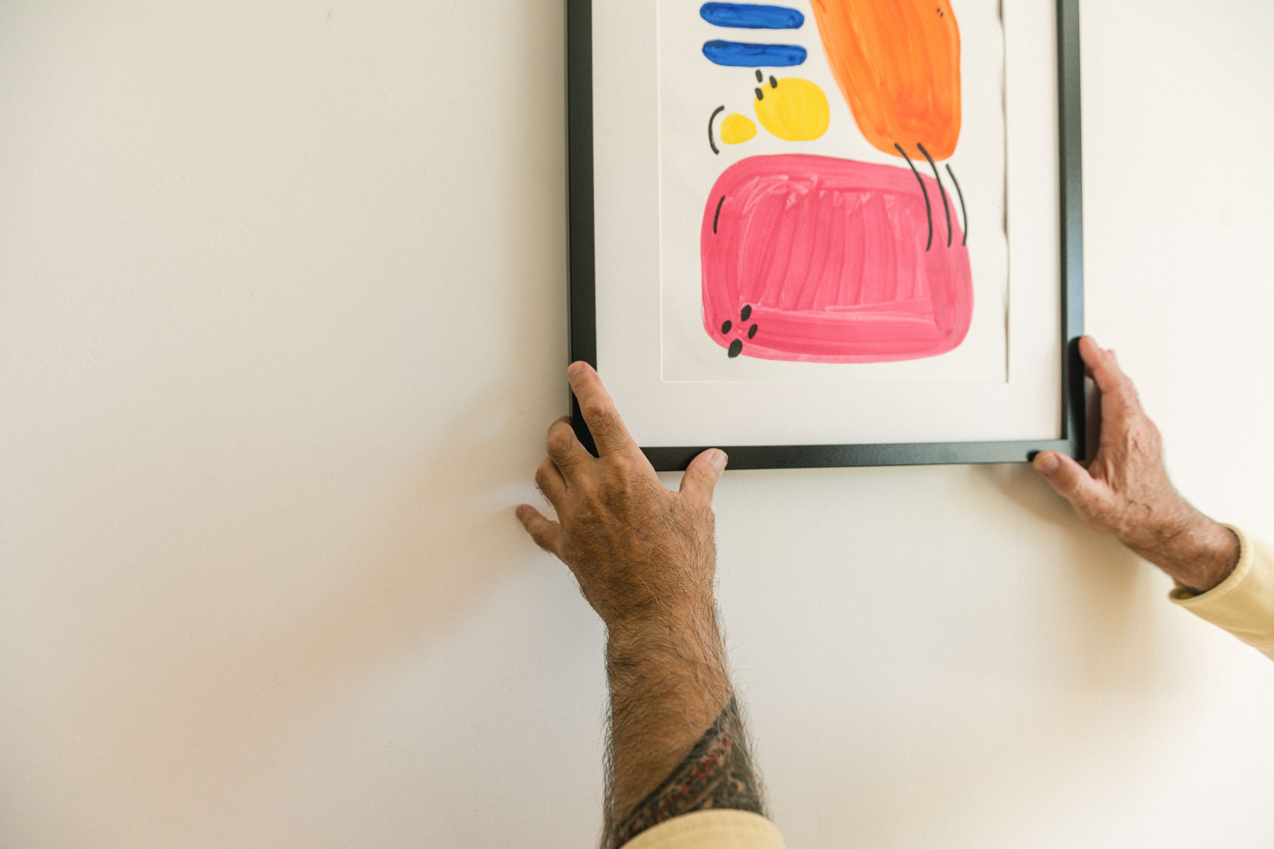 Mains tatouées suspendant tableau abstrait coloré
